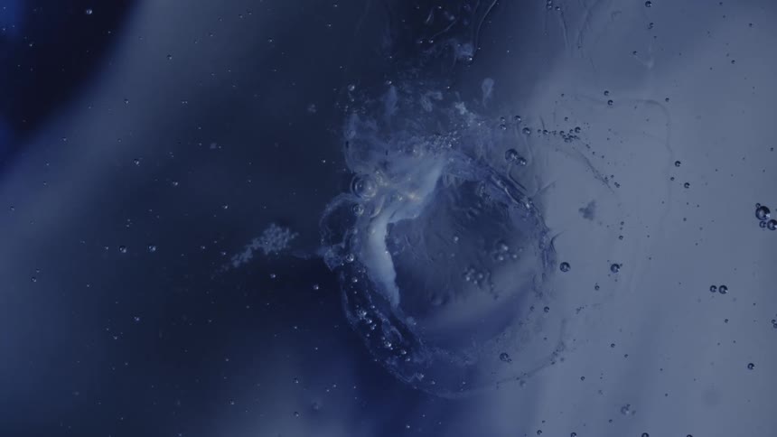 Closeup of an abstract circular air bubble forms and ripples across a dark blue liquid surface