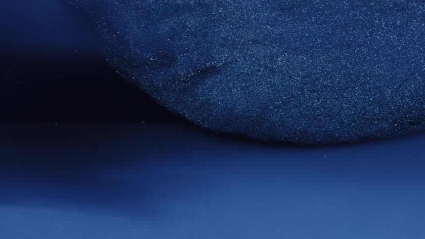 Glittering blue liquid slowly flows and swirls into a deep blue fluid creating a shimmering abstract motion