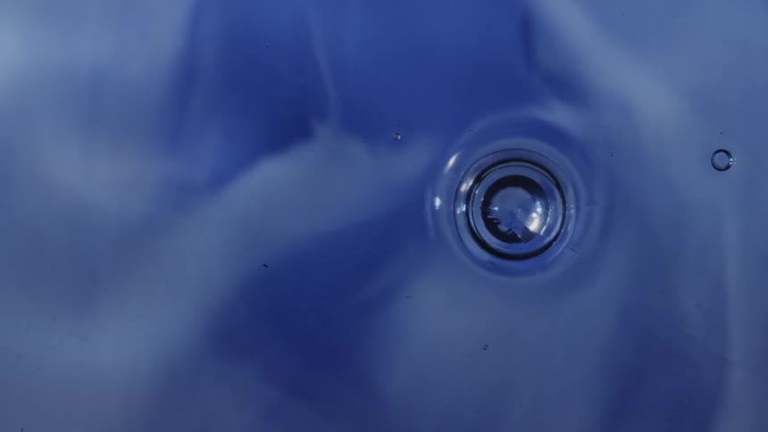 A soft abstract blue field fills the frame as a translucent spherical droplet floats near the center subtly distorting the surrounding fluidlike forms and light reflections to create a serene dreamlike visual