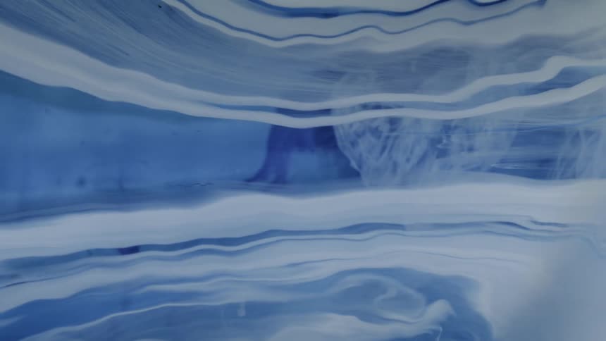 Blue and white ink swirls together in a liquid to form marble like patterns and flowing textures