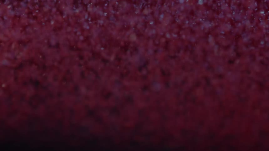 Closeup of dense red glitter cascading creating a shimmering abstract texture against a dark background