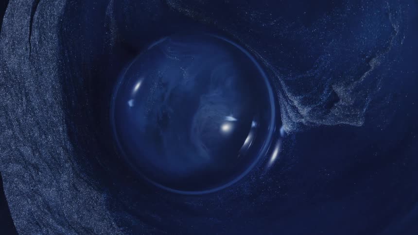 Closeup of a dark blue liquid forming a bubble with textured particles swirling around