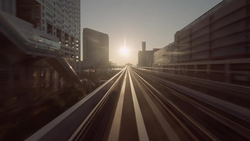 A highspeed timelapse captures the yurikamome line monorail surging toward odaiba at sunset blurring past modern skyscrapers as it chases the golden light along the elevated track