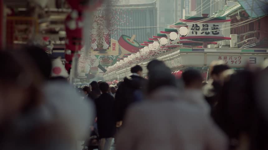 Shoppers move along a bustling city market street with colorful shop signs in the daytime