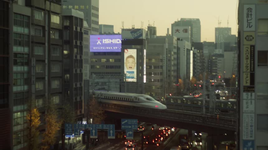Trains going through a flyover railway with a street and heavy traffic underneath on a metropolitan area outdoors during dusk or dawn
