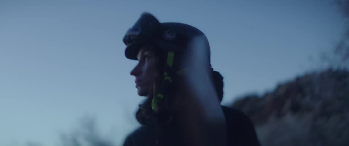 Young adult woman wearing helmet and goggles holding a snowboard and looking around with a nervous facial expression outdoors