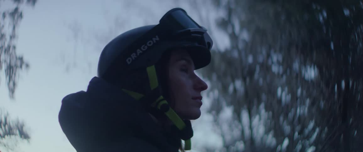 Person in profile wears a helmet and protective goggles in an outdoor setting with blurred trees in the background