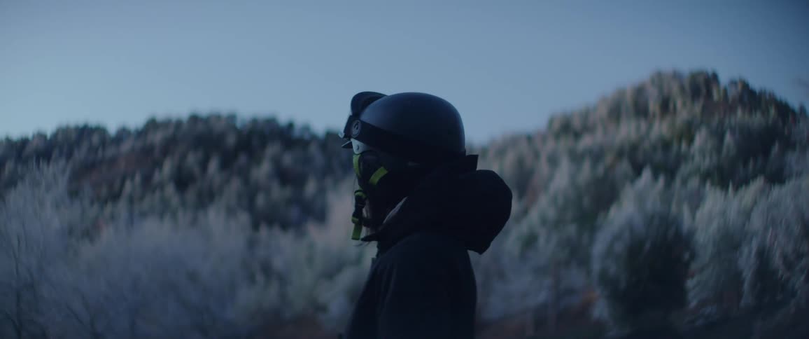 Woman wearing a crash helmet and goggles stands near frost covered trees on a winter day
