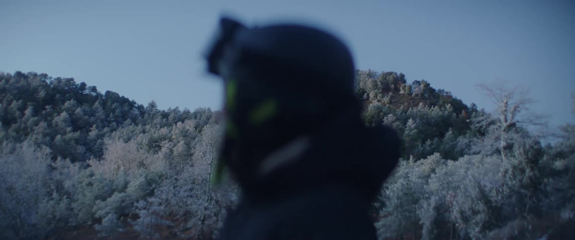 Person in the foreground appears out of focus in front of a treecovered hillside under a clear sky