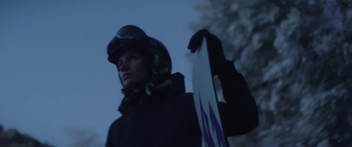 Woman holding a snowboard stands near frost covered trees on a winter day
