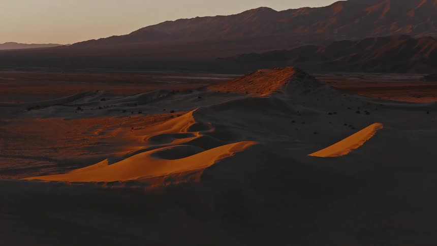 Sunlight glows on rolling sand dunes against a mountain backdrop