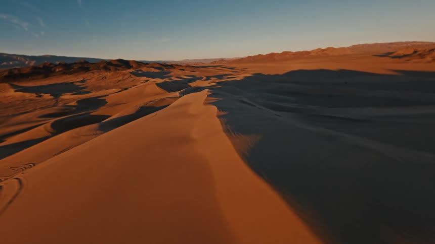 A fastmoving perspective sweeps low across endless sand dunes capturing the sharp contrast between the sunlit orange crests and the cool dark valleys below