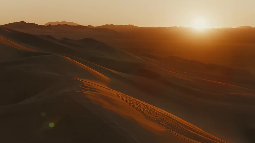 Sand dunes across the desert as the sun shines brightly over mountains in the distance