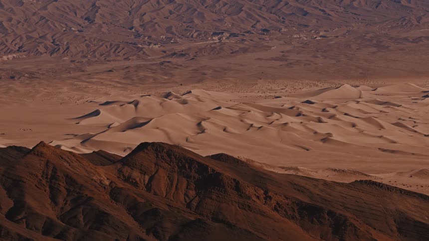 An expansive desert landscape unfolds with rolling sand dunes and layered rocky ridges stretching into the distance their warm earth tones and rippled textures highlighting the vast arid beauty of the terrain