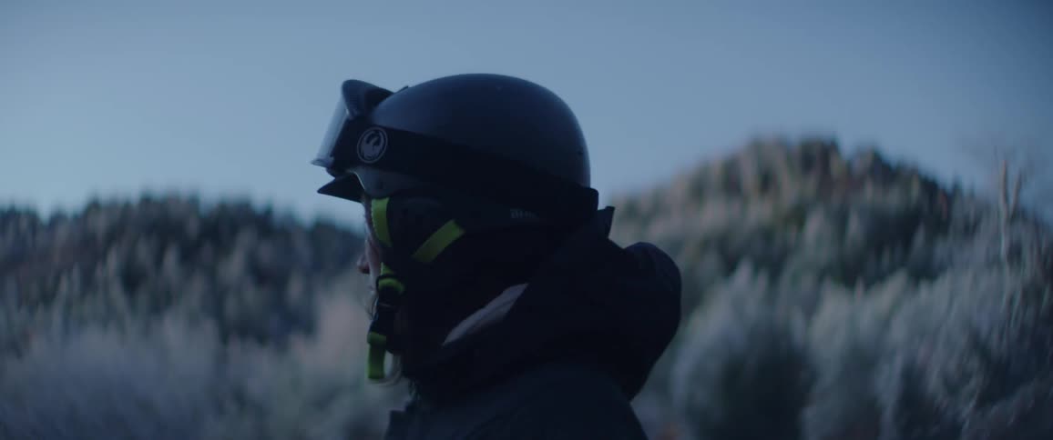 A person wearing a helmet stands in tall grass and gazing across the landscape at dusk
