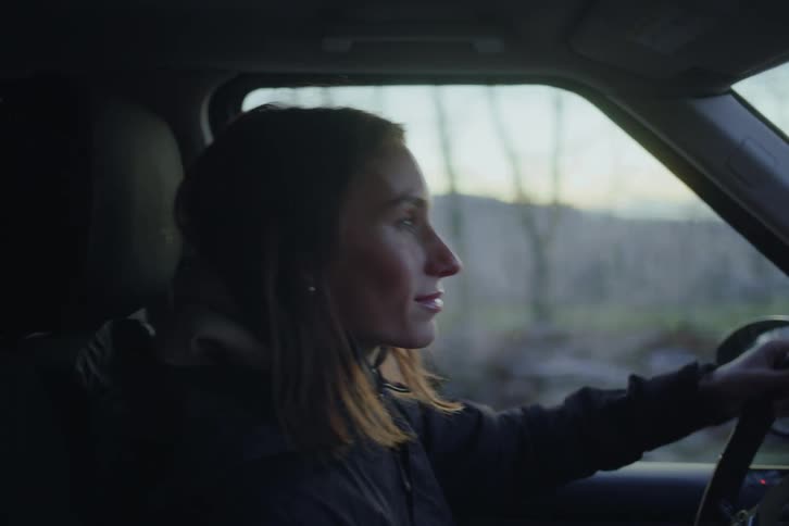 Woman drives a vehicle seen in profile from inside the car with a blurred landscape in the background