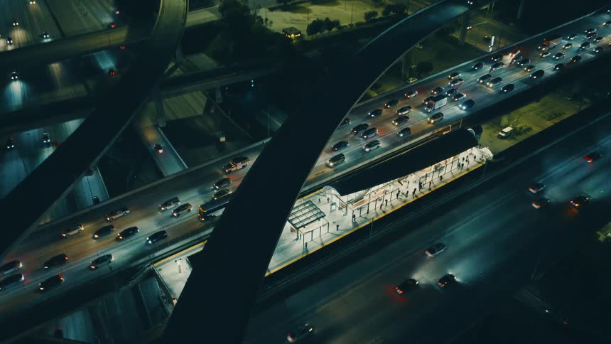 People at a station in the middle of a stack interchange with heavy traffic on a metropolitan area outdoors during night time