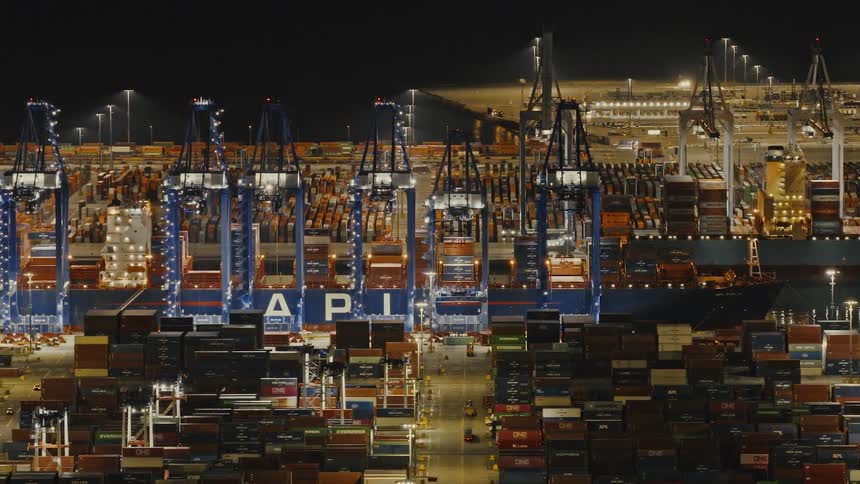 Slow aerial tracking shot gliding past busy cargo terminal at Port of Long Beach at night