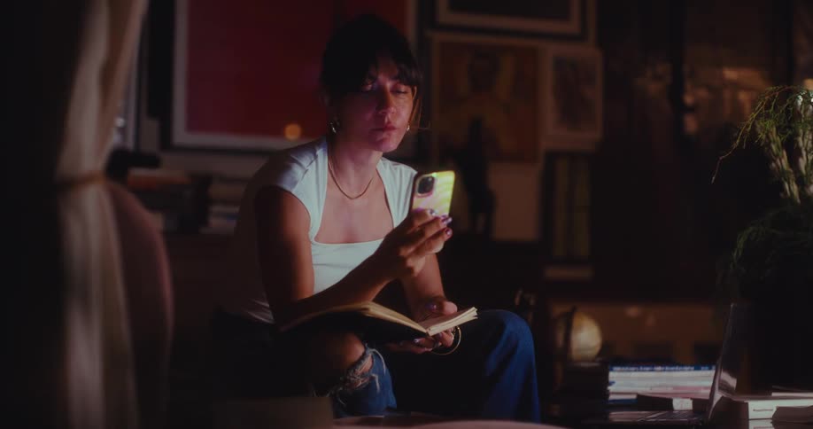 A woman writing in a notebook while sitting indoors in a dimly lit room