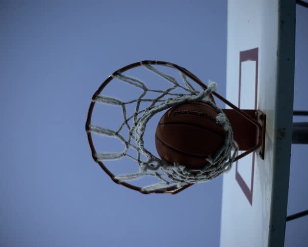 A basketball dropping through the hoop at midday slipping out of the net