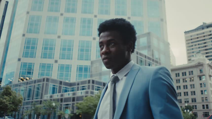 Man standing on a downtown street as he looks up and walks forward
