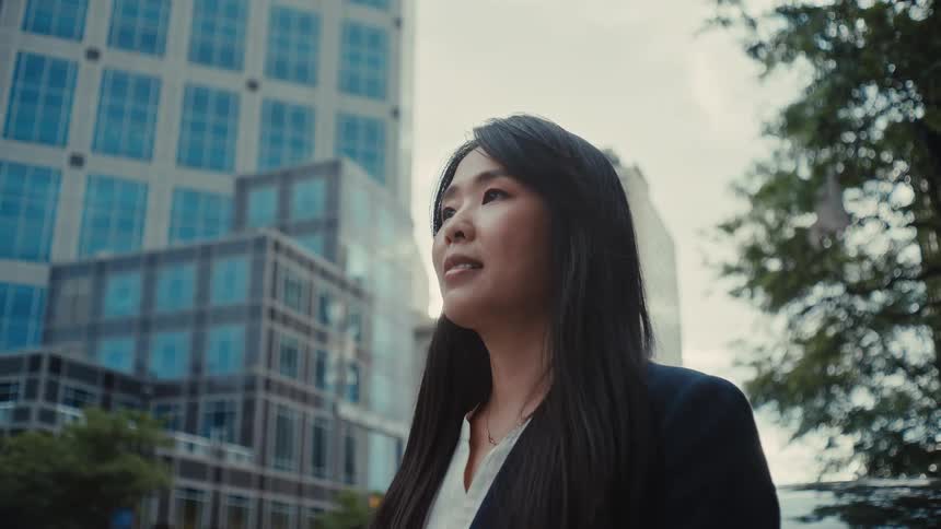 Asian adult female standing on a street of a metropolitan area then smiling and walking away outdoors during day time