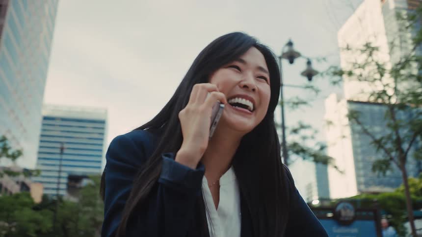 Asian young adult female laughing while talking on the phone on a metropolitan area during day time