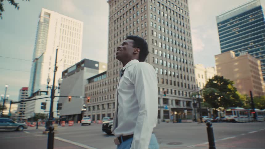 Man in business attire looks up at tall buildings at an urban intersection during daytime
