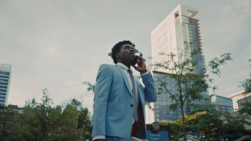 Man in business attire talks on the phone in an urban area surrounded by buildings and street lamps