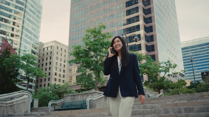 Woman walks down stairs near downtown buildings talking on her phone