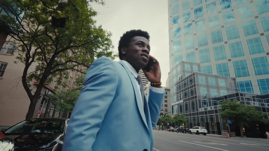 Man closes his car door on a city street as he talks on his phone and walks away