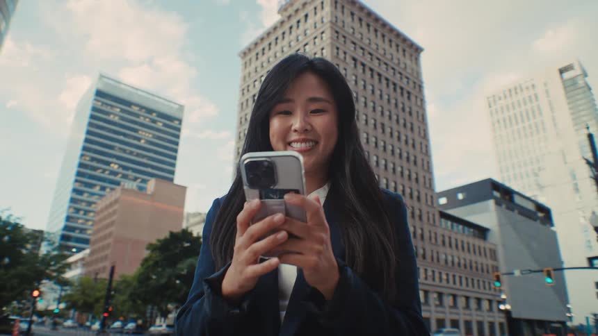 The woman is smiling while she texts in the city