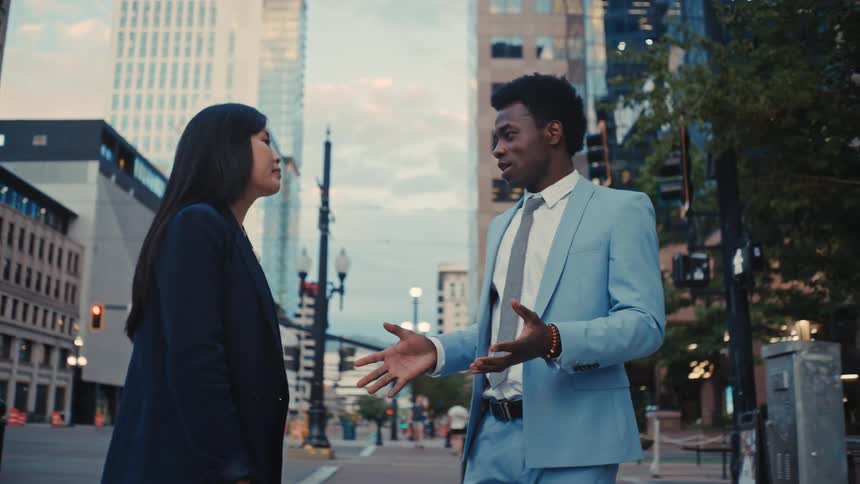 Man and a woman in formal attire chatting outdoors in the city