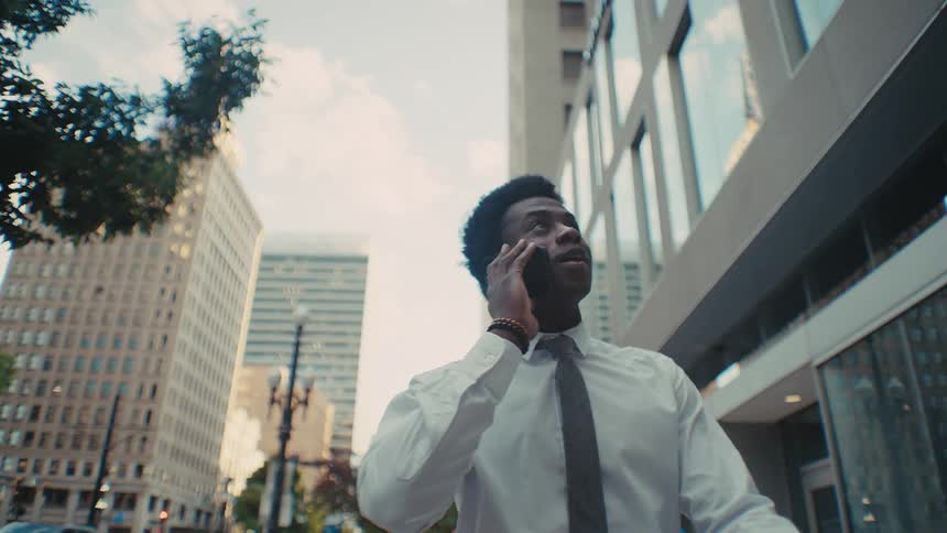 Man walks in front of downtown buildings as he talks on his phone