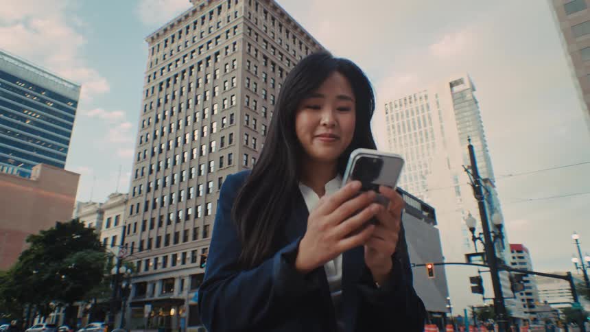 The woman is looking at her phone on the street corner