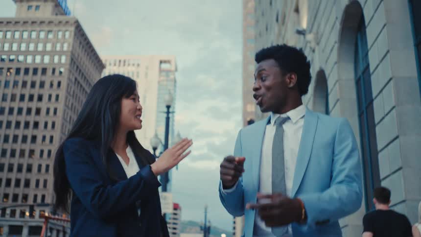 A man and woman smile as they talk and walk down a city street