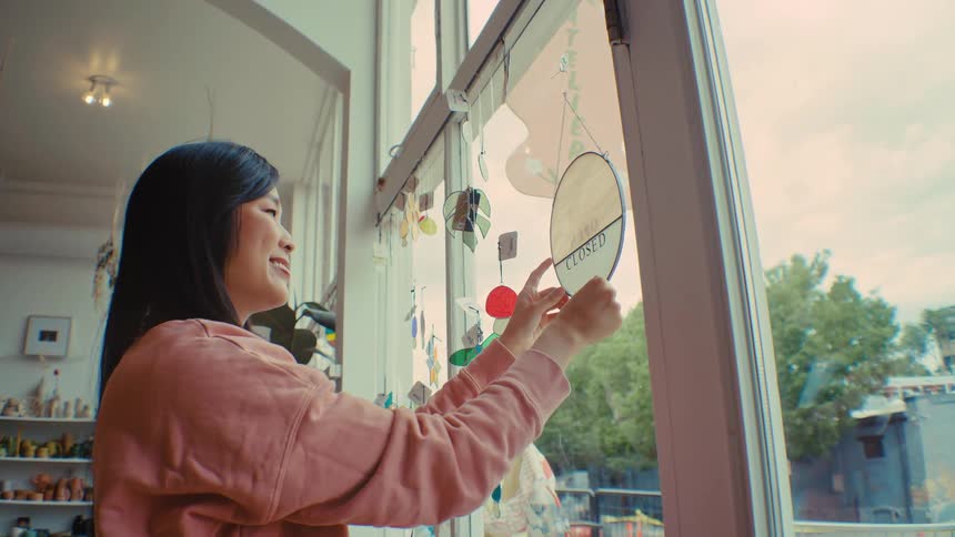 A woman flipping a sign to open in a store