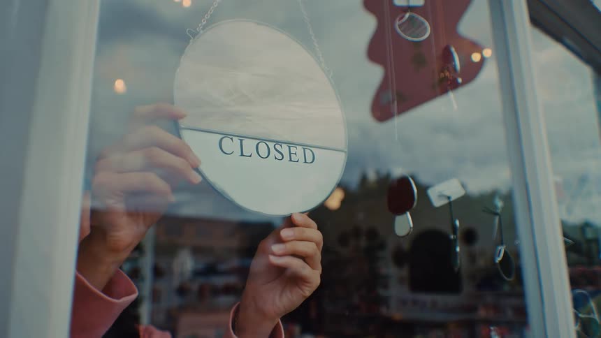 Woman turns over the open sign in her store window to closed