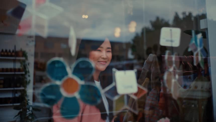 A shopkeeper arranges a vibrant display behind a glass window with city street reflections