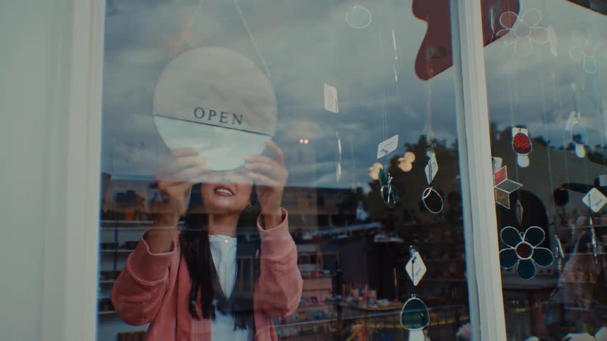 Woman turns over the sign in her store window to open