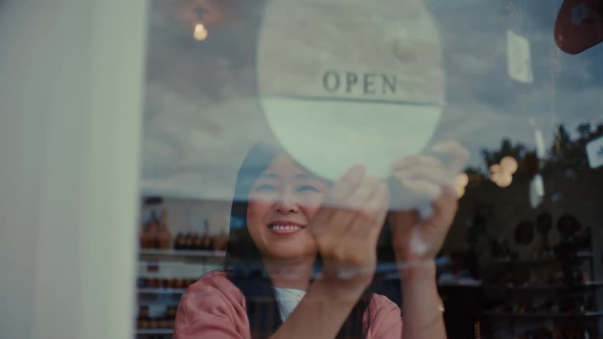 Smiling woman opening a shop with a sign