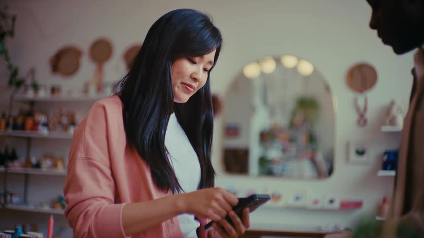 A woman laughs as she taps a credit card against a smartphone in a boutique