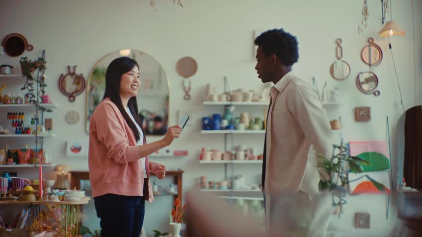 Woman hands a card to a man inside a shop with product shelves in the background