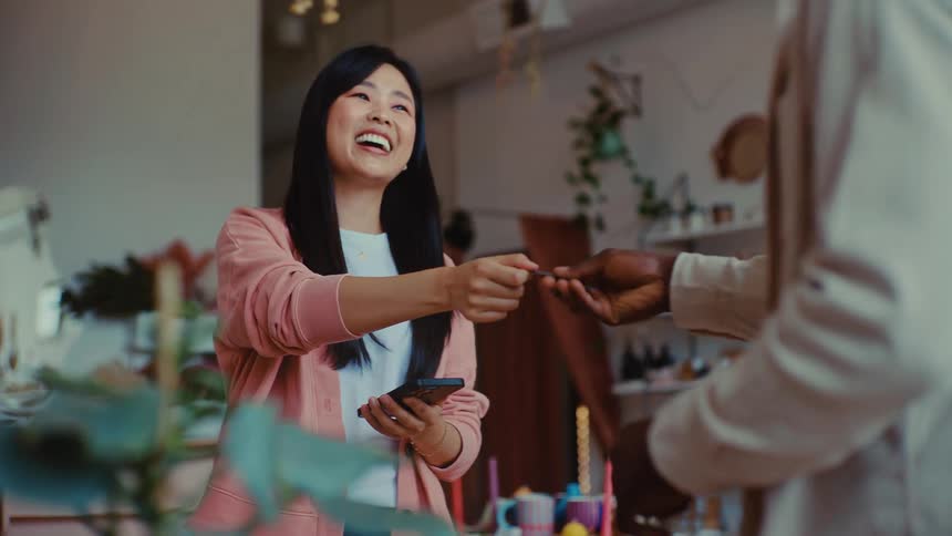 A woman smiles and laughs while processing a credit card payment on her smartphone in a boutique