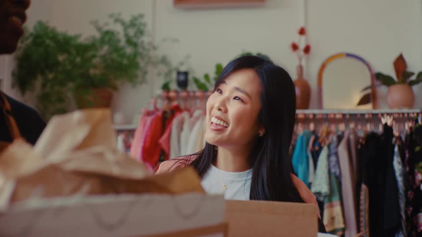 Retail coworkers have a friendly conversation while holding packages in a clothing store