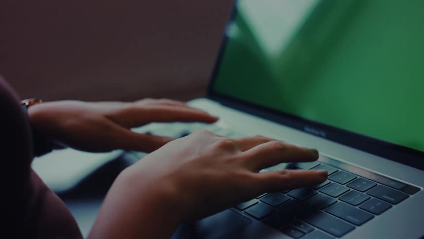 A persons hands are shown typing on a laptop with a green screen