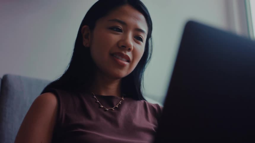 Woman types on a laptop while seated in an indoor setting with soft light