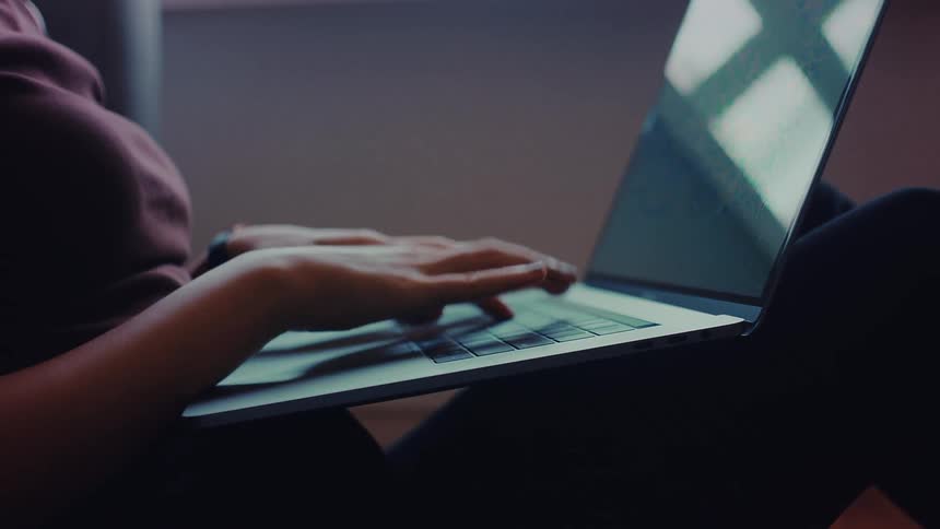 A woman wearing a red shirt sitting with a laptop on her lapas she typs on it
