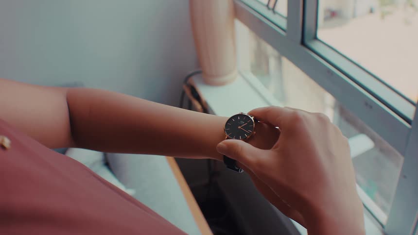 Person adjusts a wristwatch near a window with natural light