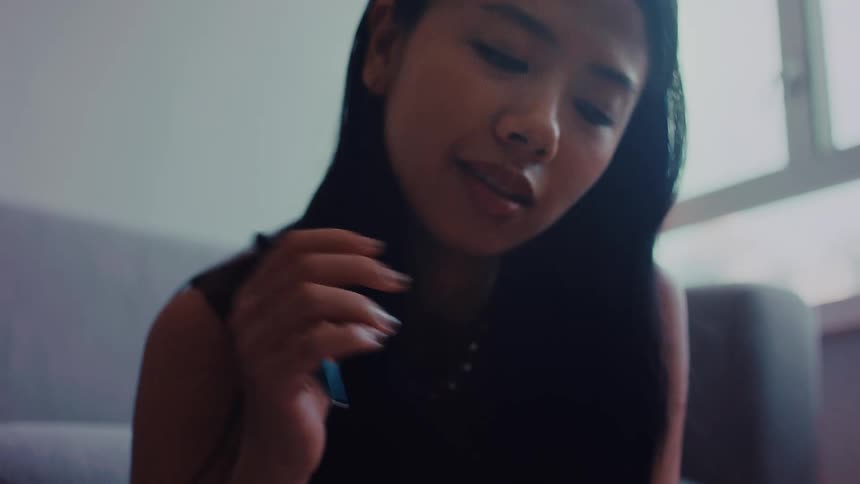 An asian woman sits on a wooden floor and writes in a notebook with a blue pen